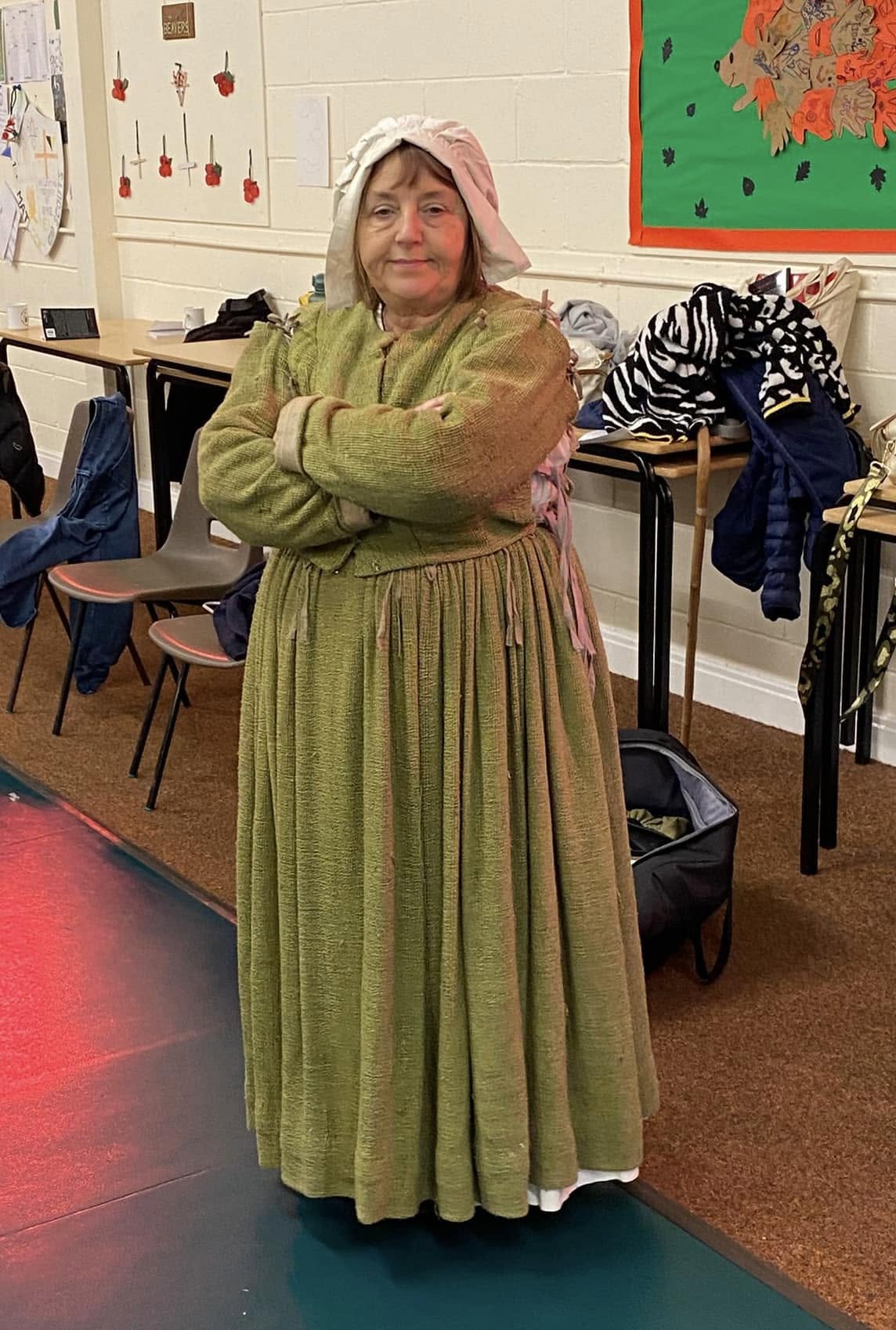 A member of The Crucible company in a green dress and bonnet