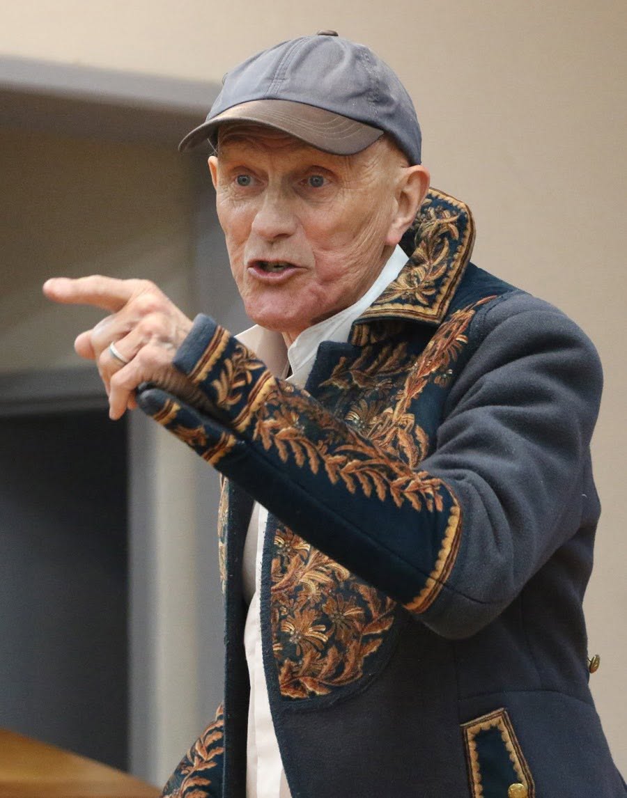 A performer in an embroidered jacket pointing across the rehearsal room